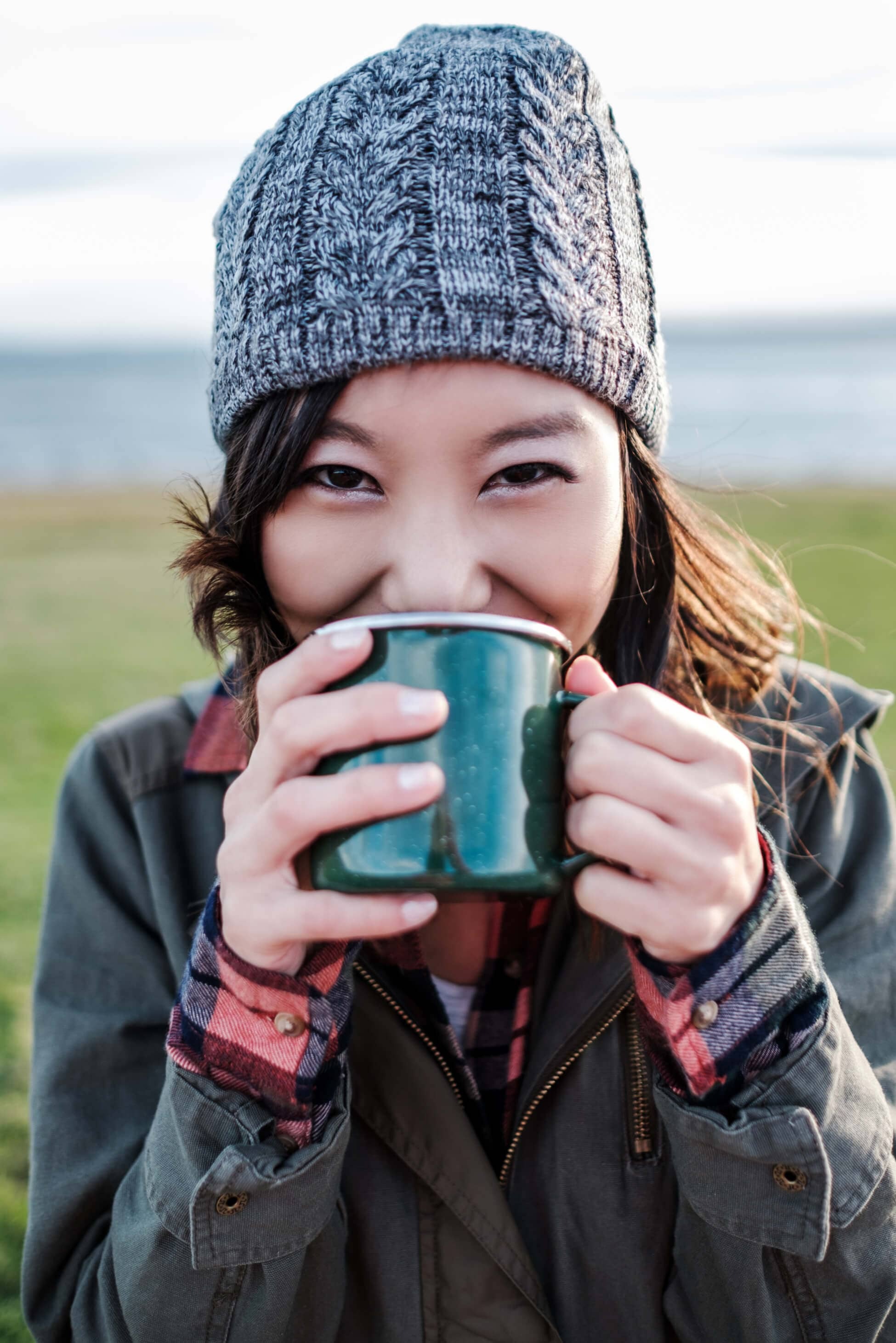 woman in a stocking cap drinking from mug outdoors